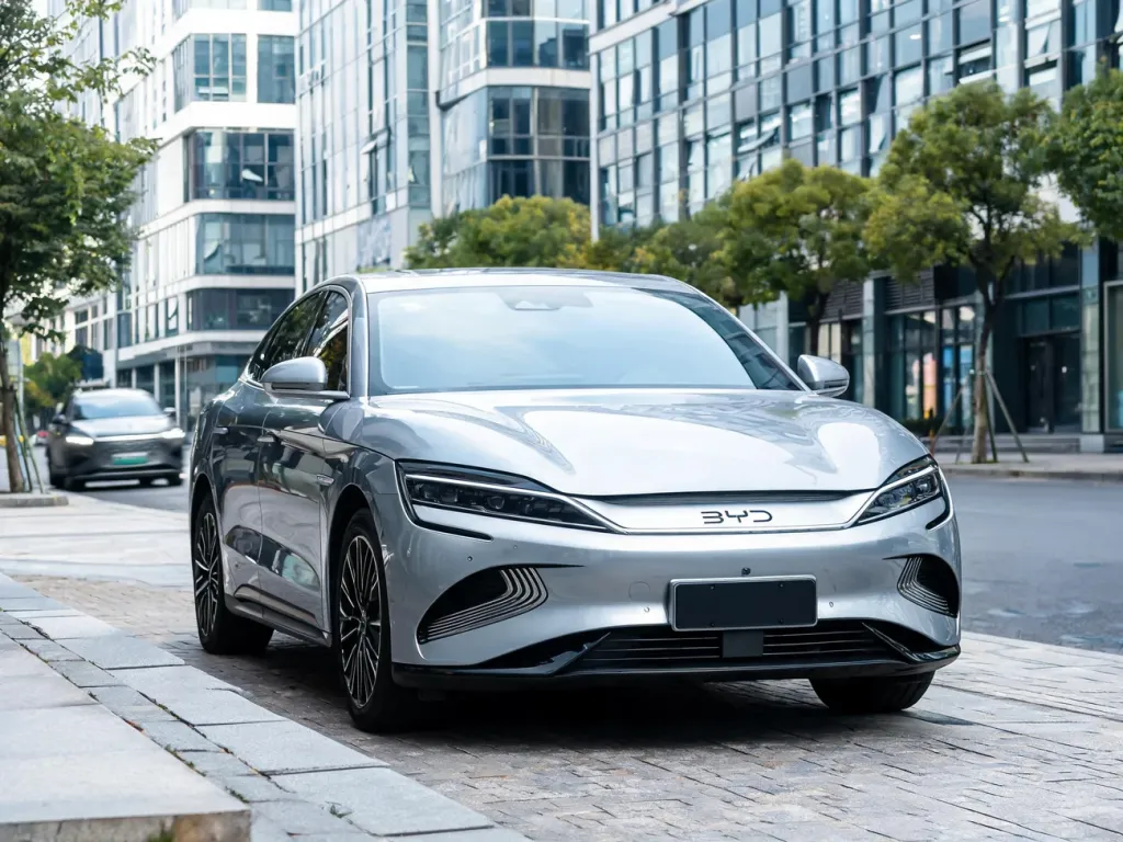 Nowoczesny elektryczny BYD w metalicznym srebrze zaparkowany na miejskiej ulicy, na tle biurowców i przejeżdżającego auta.